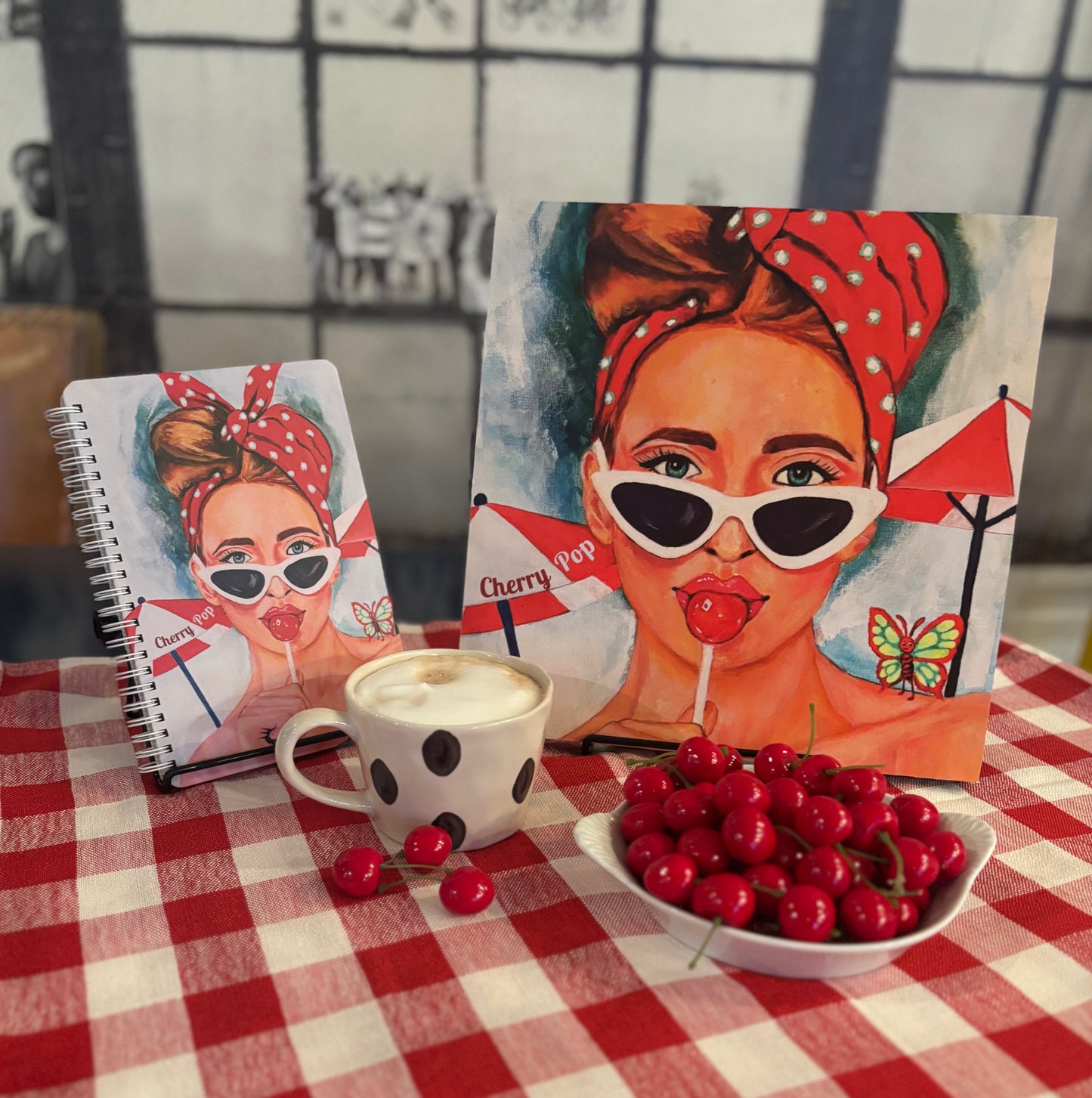 Cherry Pop art notebook featuring a retro red-haired girl illustration, styled beside a matching 12×12 art print with a latte and a bowl of cherries; colorful 60s Charmers aesthetic notebook photo.