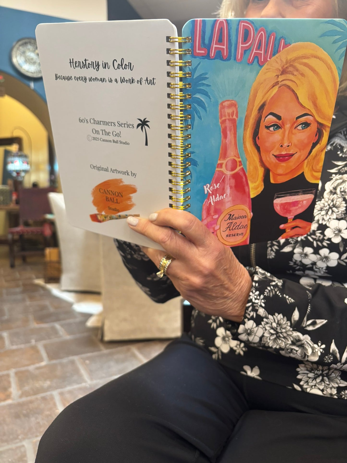 Person holding a notebook with a vintage-style illustration of a woman and a bottle on the cover.
