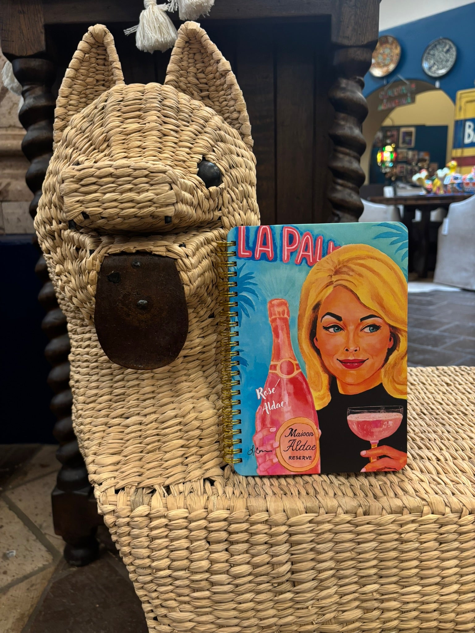 Notebook with a colorful cover featuring a woman and a bottle, placed on a woven surface.