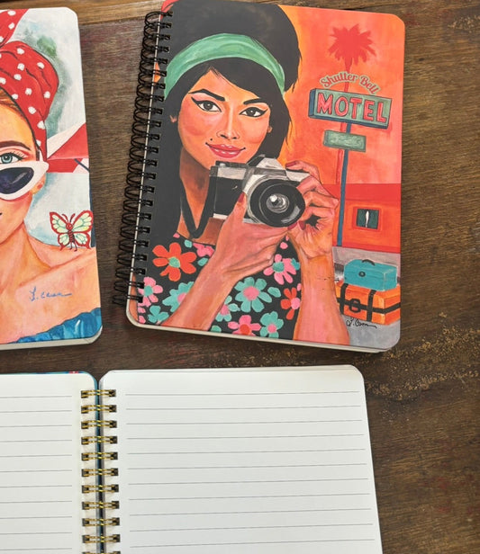 Notebook with a colorful retro illustration of a woman holding a camera on a wooden surface