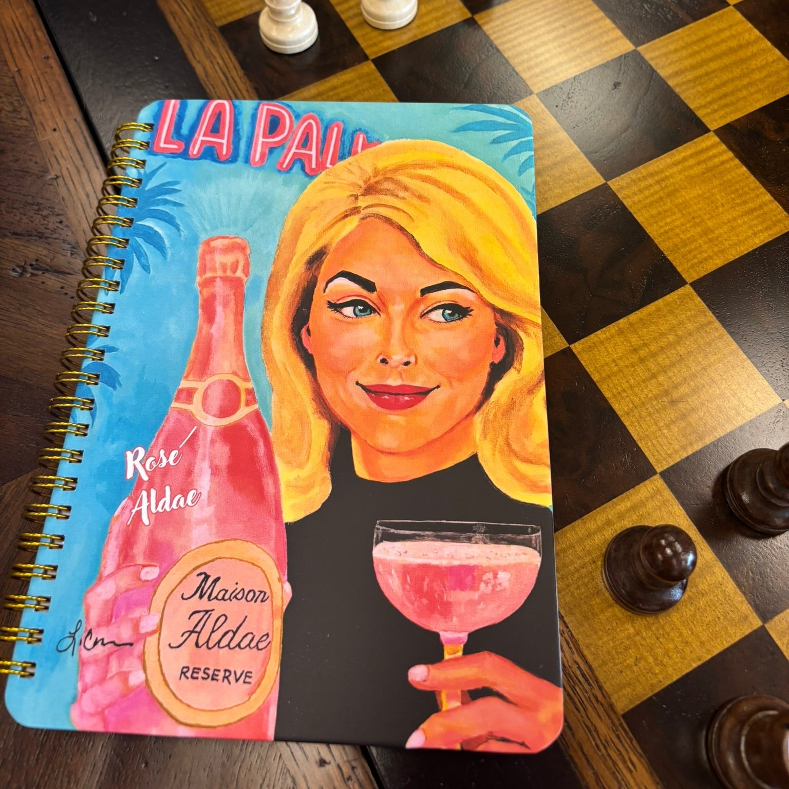 Glamorous art notebook featuring a blonde woman holding rosé; stylish retro-inspired journal with bold feminine artwork.