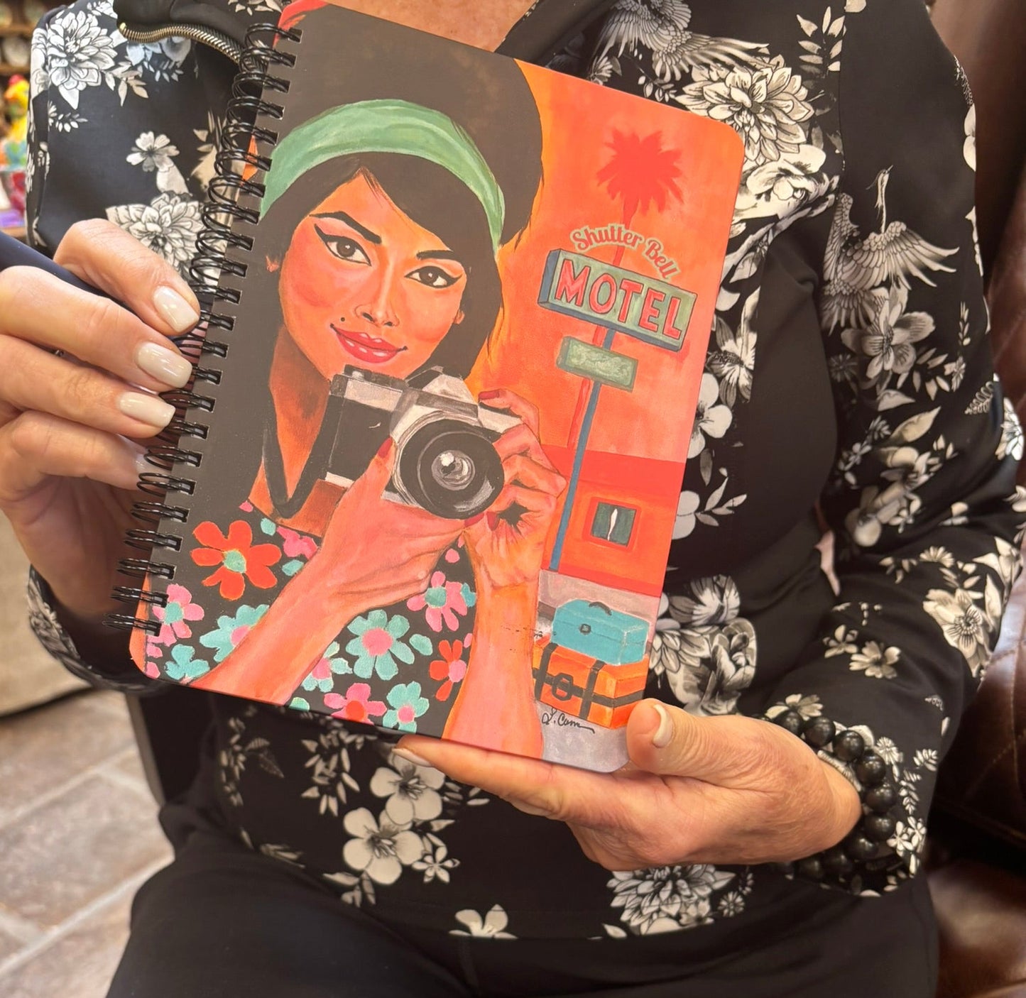 Person holding the Shutter Bell art notebook featuring a retro camera girl illustration; lifestyle photo highlighting the notebook’s design and size.