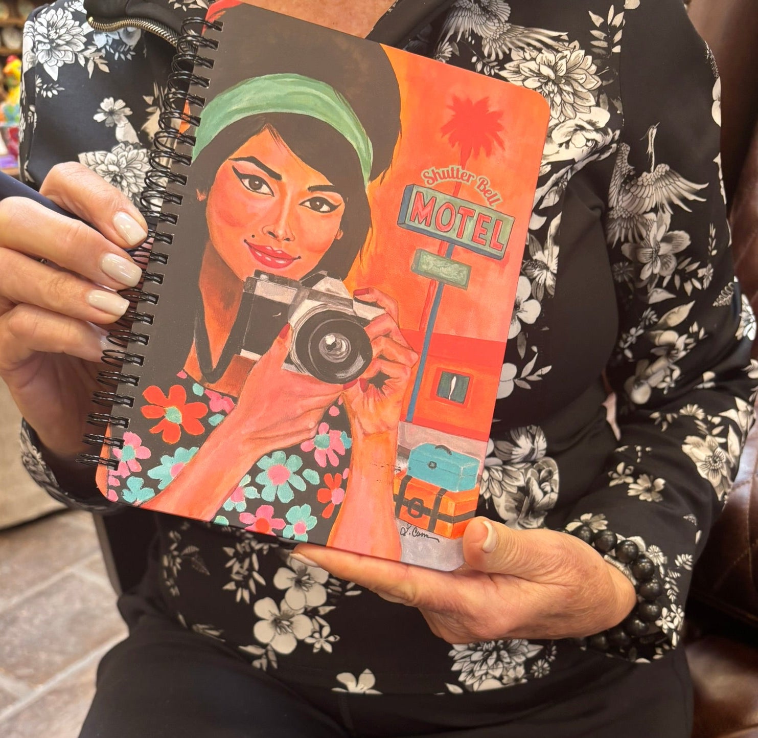 Person holding the Shutter Bell art notebook featuring a retro camera girl illustration; lifestyle photo highlighting the notebook’s design and size.