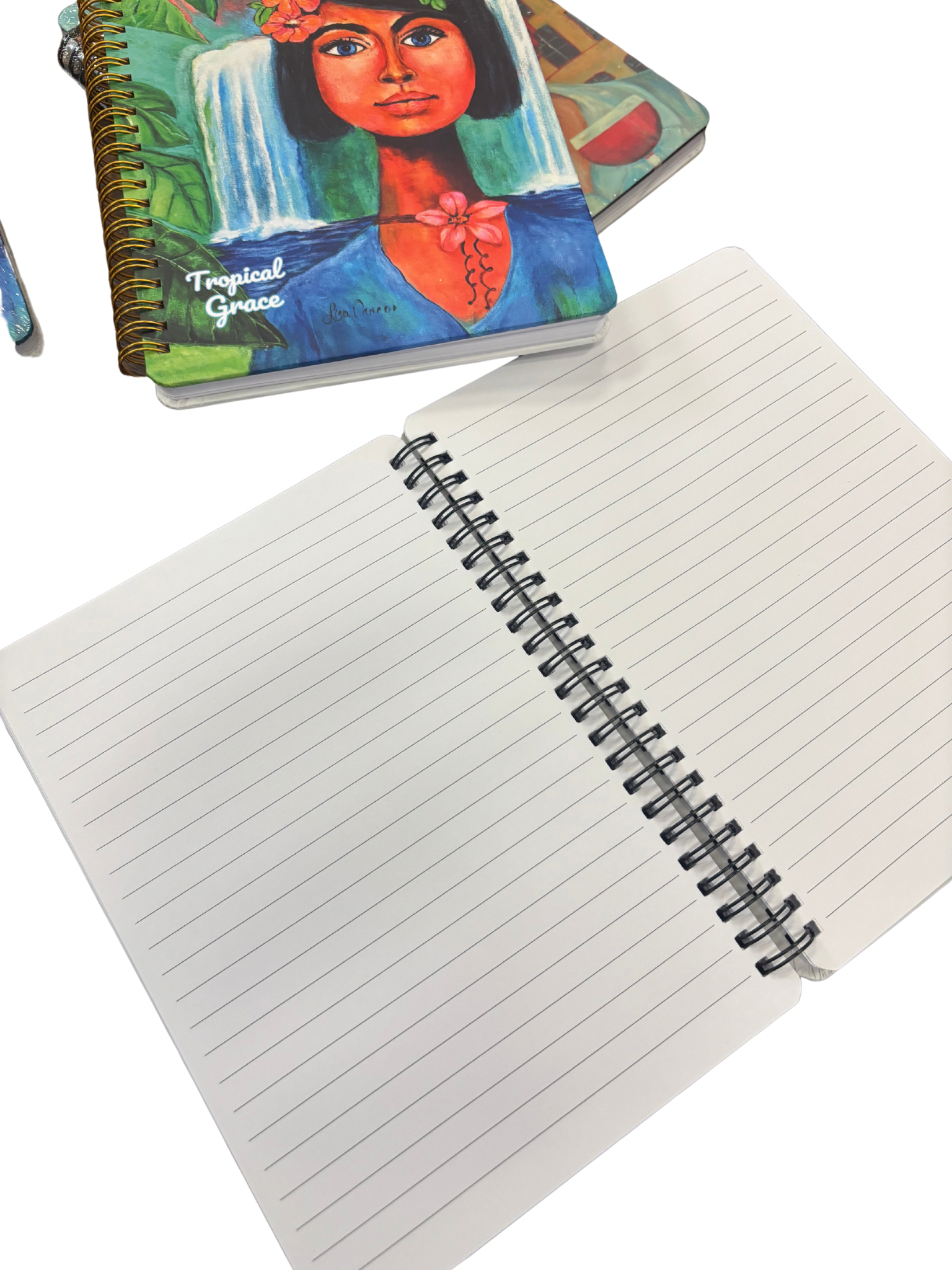 Open lined notebook showing interior pages with the Tropical Grace art notebook placed above it; feminine illustrated journal from the Femmes & Feathers collection displayed in a lifestyle photo.